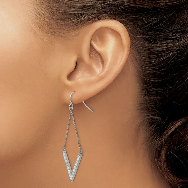 A woman wearing a long silver V-shaped dangle earring with a textured finish on a fish hook ear wire.