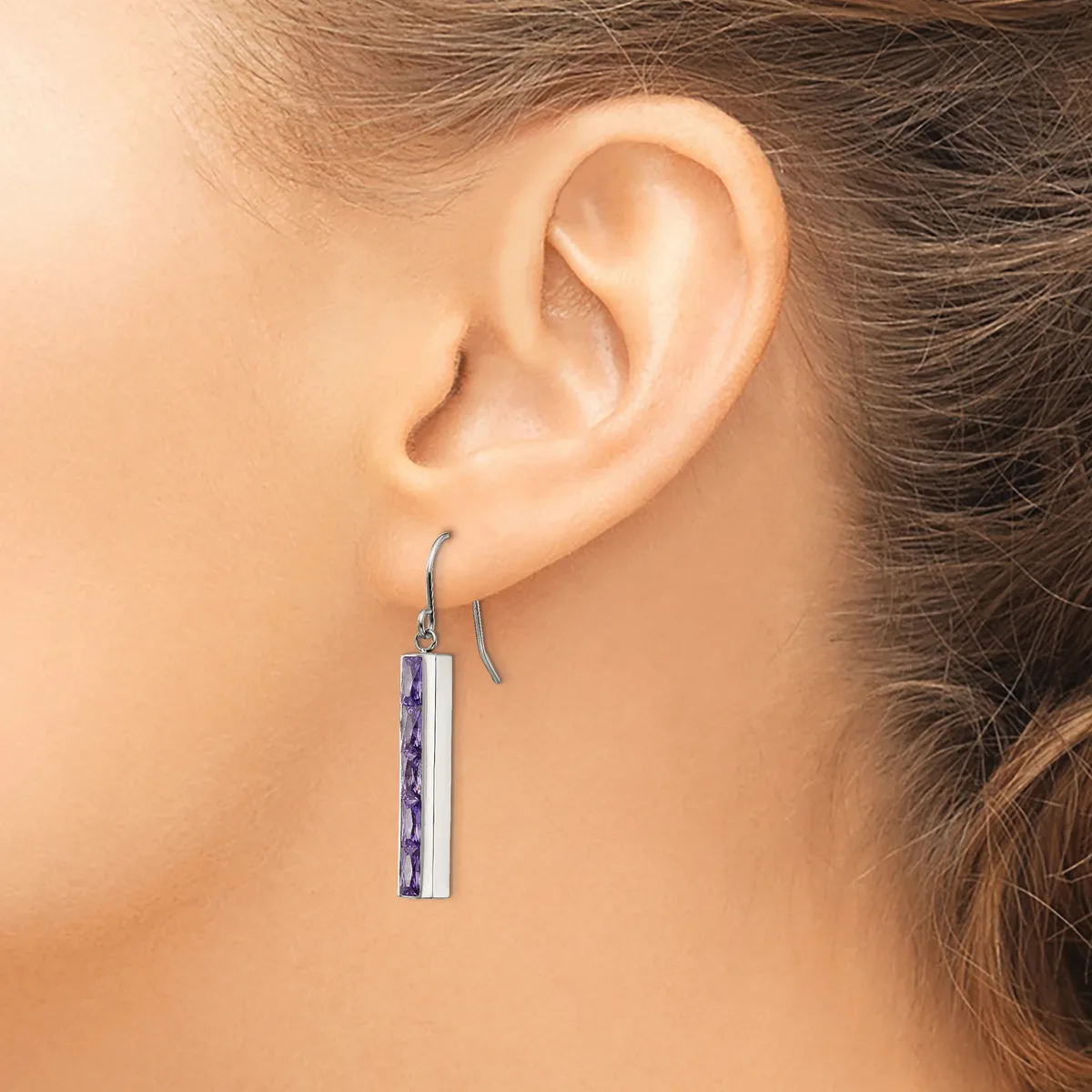 A person wearing a rectangular pendant earring with purple and white striped inlay hanging from a curved silver wire hook.