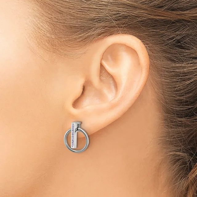 A silver-toned circular earring with a vertical bar detail worn on a person's earlobe.