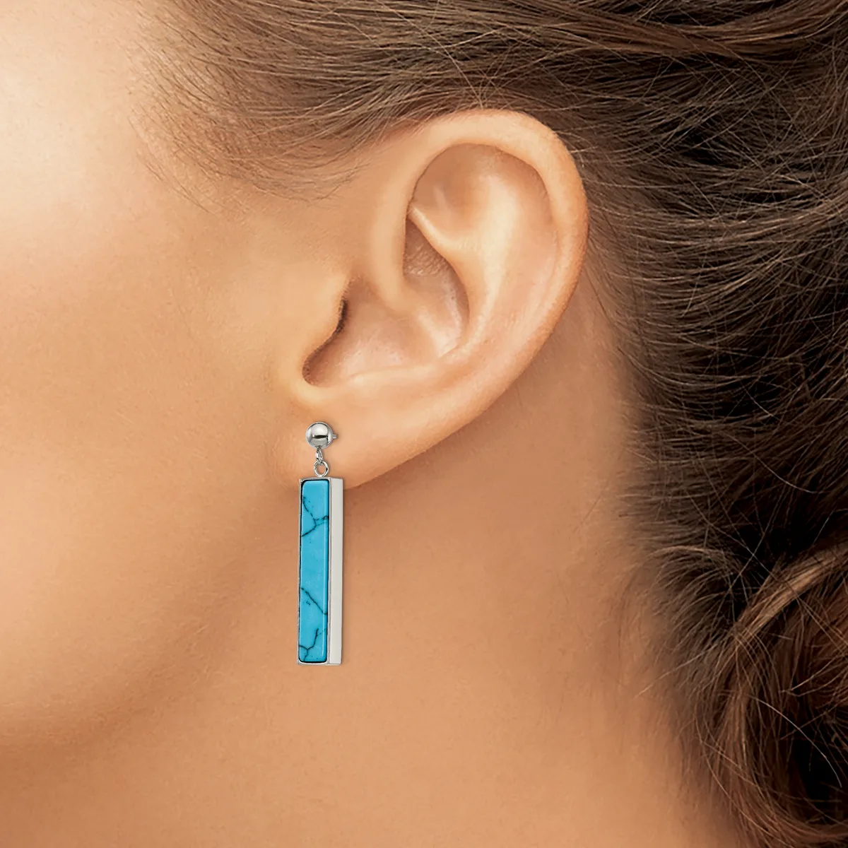 A person wearing a long rectangular turquoise pendant earring with dark veining, hanging from a small silver post stud.