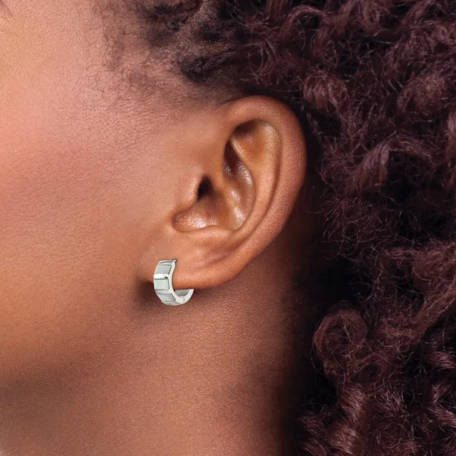 A person wearing a polished silver chunky hoop earring in their earlobe, shown in profile with dark curly hair visible.