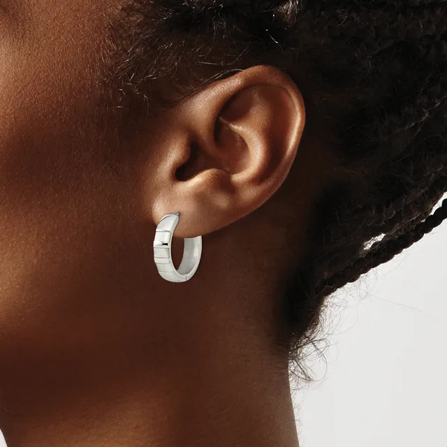A person wearing a polished silver hoop earring with a textured band, shown from the side view of their ear and neck.