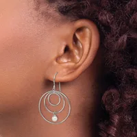 A person wearing a silver wire dangle earring with three concentric circular loops and a small pearl hanging from the innermost loop.