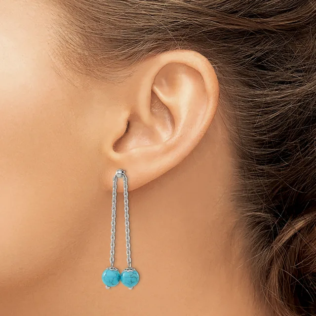 A person wearing long dangling earrings with turquoise blue spherical stones suspended from thin silver chain threaded through pierced earlobes.