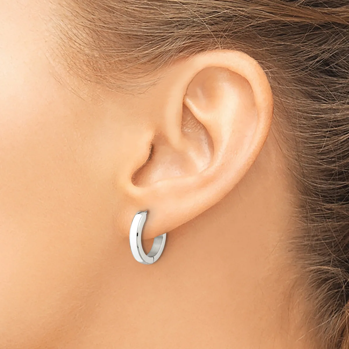 A person wearing a polished silver hoop earring in their pierced earlobe, shown from the side profile.