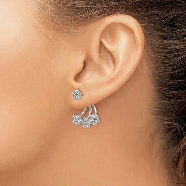 A person wearing two diamond stud earrings in one ear and a chandelier-style earring with three diamond drops hanging from curved silver bars.