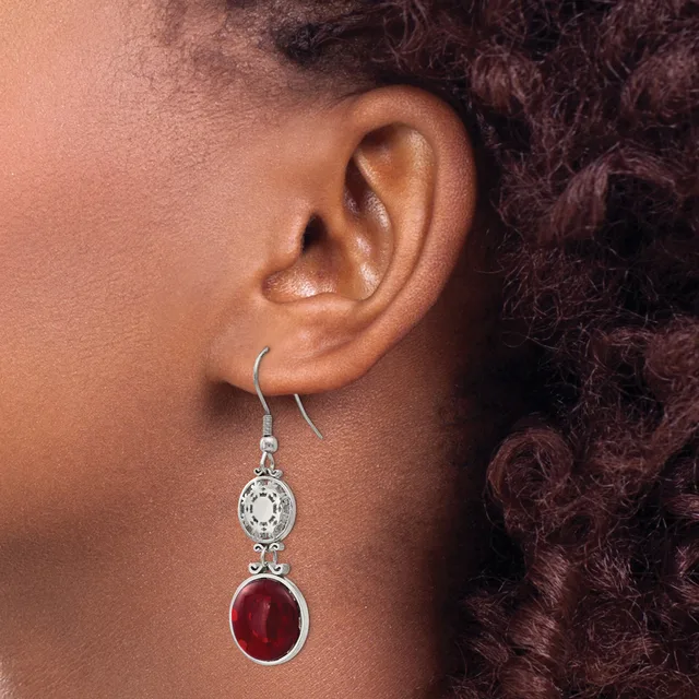 A person wearing silver drop earrings with an oval white gemstone on top and a round red stone below, shown from the side against dark hair.