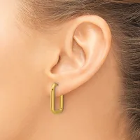 A person wearing a pair of gold-toned rectangular hoop earrings with rounded corners, shown from the side view of their ear.