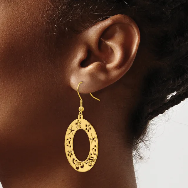A person wearing gold-toned oval drop earrings with decorative cutout patterns, shown from the side profile against a neutral background.