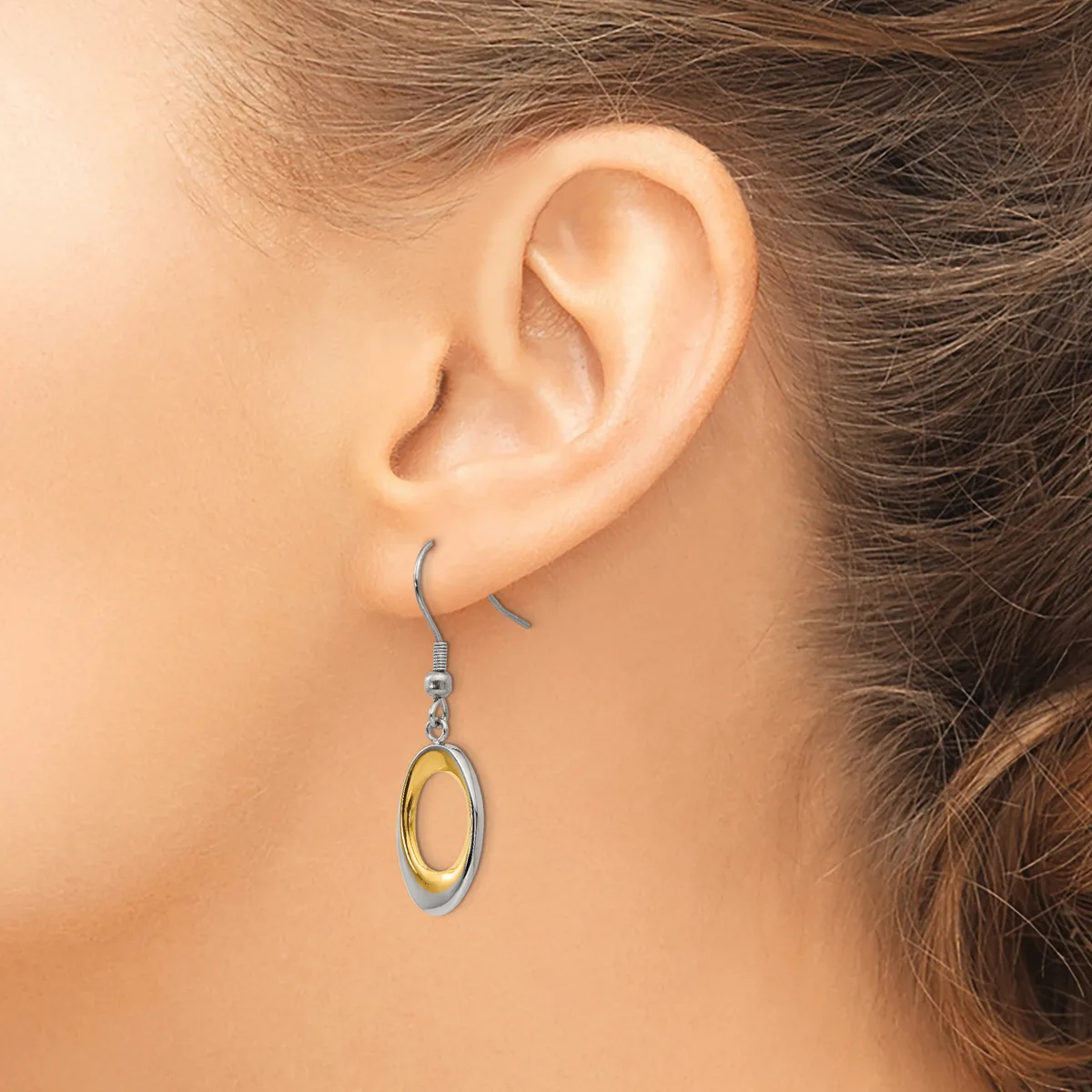 A woman wearing a two-tone oval dangle earring with a silver outer ring and gold inner oval, suspended from a silver ear wire.