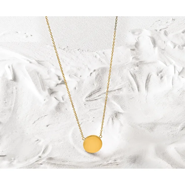A gold chain necklace with a round yellow pendant displayed on a textured white surface.