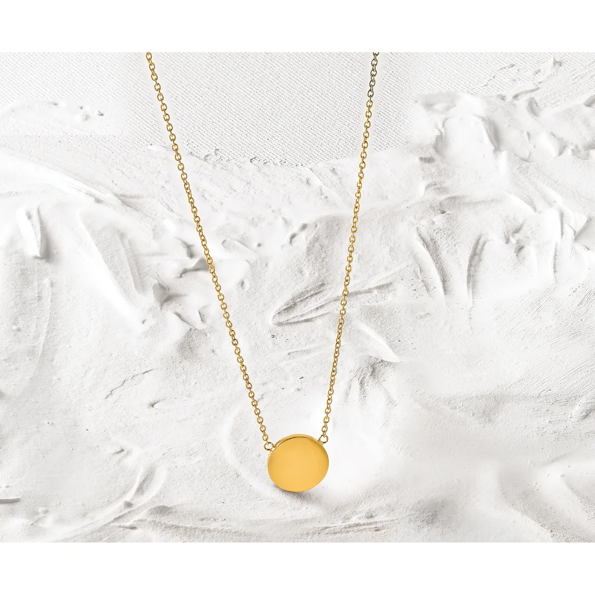 A gold chain necklace with a round yellow pendant displayed on a textured white surface.