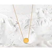 A gold chain necklace with a round yellow pendant displayed on a textured white surface.