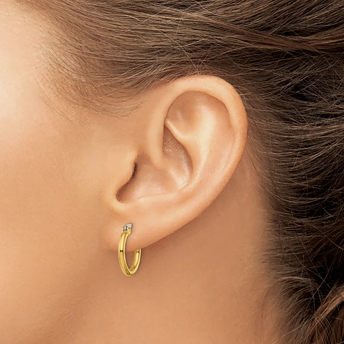 A close-up side view of a person's ear wearing a small gold hoop earring with a gemstone accent.