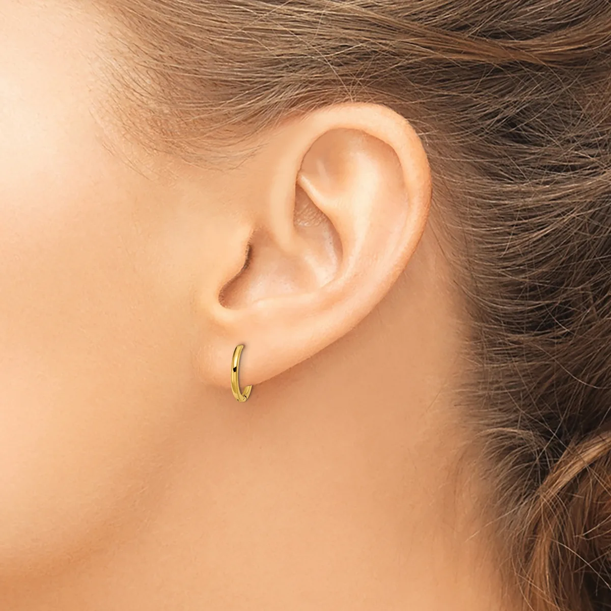A person wearing a small gold hoop earring in their earlobe, shown in profile with brown hair pulled back.