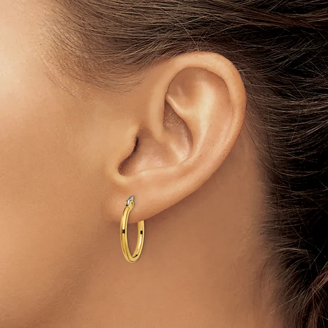 A person wearing small gold hoop earrings, shown from the side with their ear and part of their face and dark hair visible.