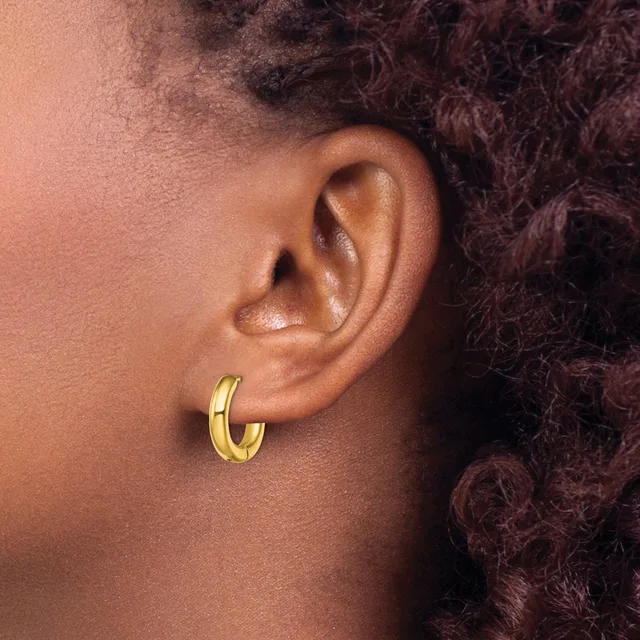 A close-up side view of a person's ear wearing a polished gold hoop earring, with dark curly hair visible in the background.