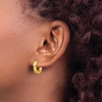 A close-up side view of a person's ear wearing a polished gold hoop earring, with dark curly hair visible in the background.