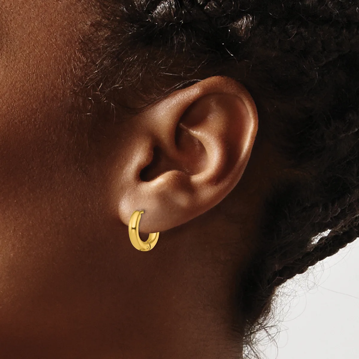 A close-up view of a person's ear wearing a small gold hoop earring with a textured surface.