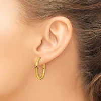 A woman's ear wearing a pair of polished gold-toned oval hoop earrings.