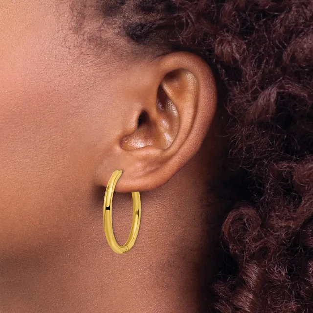 A person wearing gold hoop earrings is shown in profile, displaying their ear and dark curly hair against a warm-toned background.