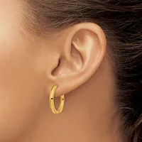 A person wearing a pair of polished gold hoop earrings, shown from the side profile of their ear and neck.