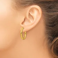 A woman wearing a pair of polished gold-toned hoop earrings, shown from the side profile of her face and ear.