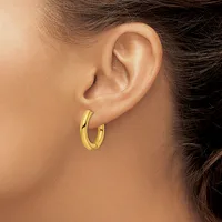 A person wearing a pair of polished gold hoop earrings, shown from the side profile of their ear and neck.