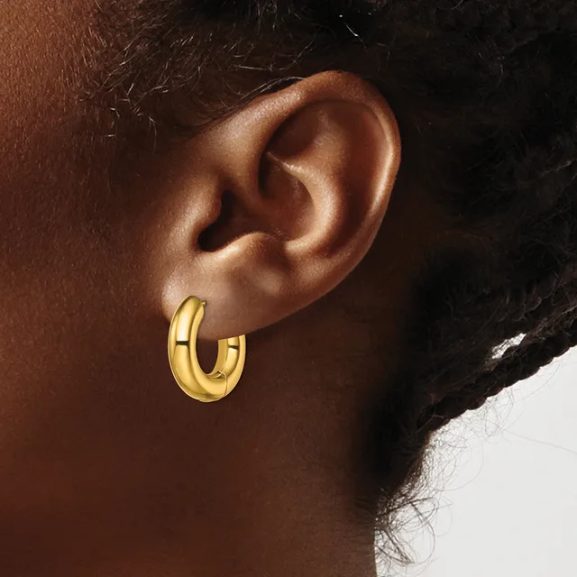 A close-up view of a person's ear wearing a polished gold-toned chunky hoop earring.