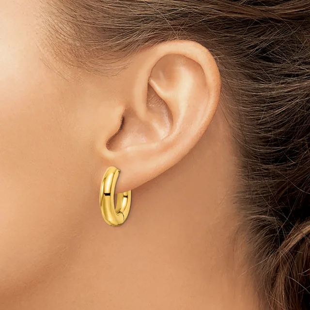 A person wearing a pair of polished gold hoop earrings with a chunky, rounded profile, shown from the side view of their ear and neck.