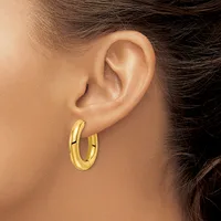 A person wearing a pair of polished gold hoop earrings with a curved, tubular design, shown from the side view of their ear.
