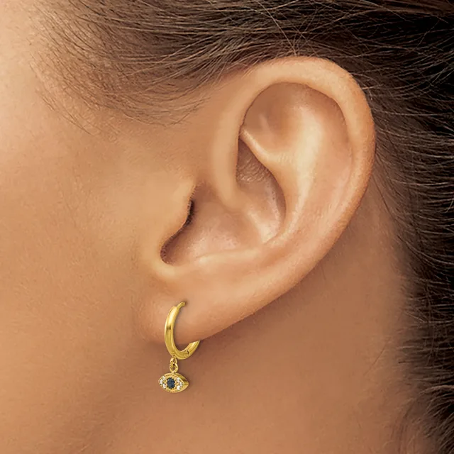 A person wearing a gold hoop earring with a small dangling charm featuring dark and clear stones, shown from the side profile of their ear.