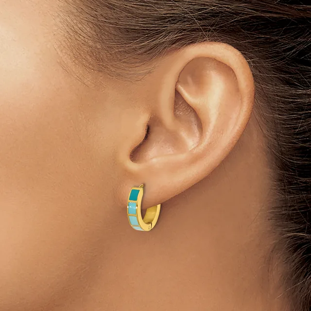 A gold hoop earring with turquoise enamel inlay worn on a person's earlobe.