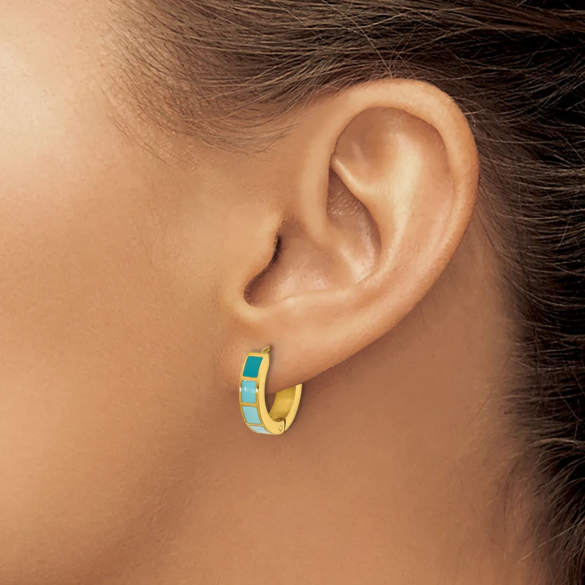 A gold hoop earring with turquoise enamel inlay worn on a person's earlobe.