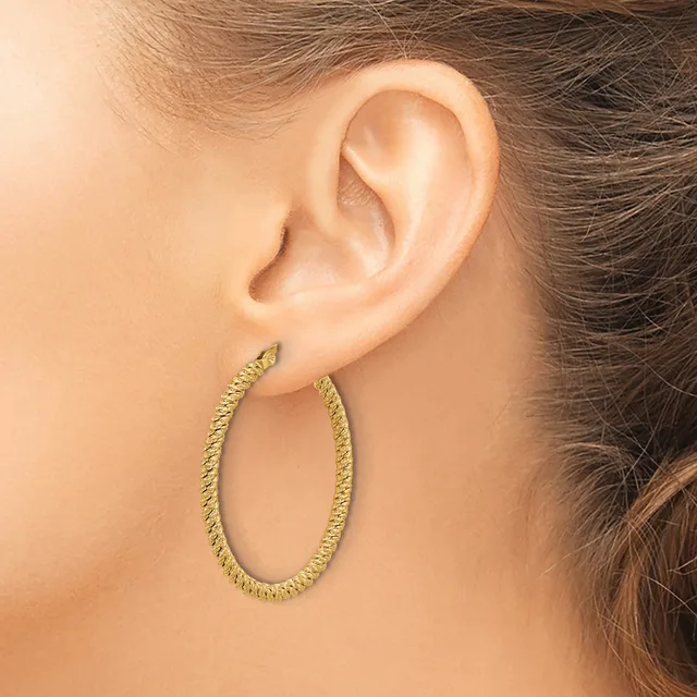 A woman wearing a large textured gold oval hoop earring in her earlobe, shown in profile view.