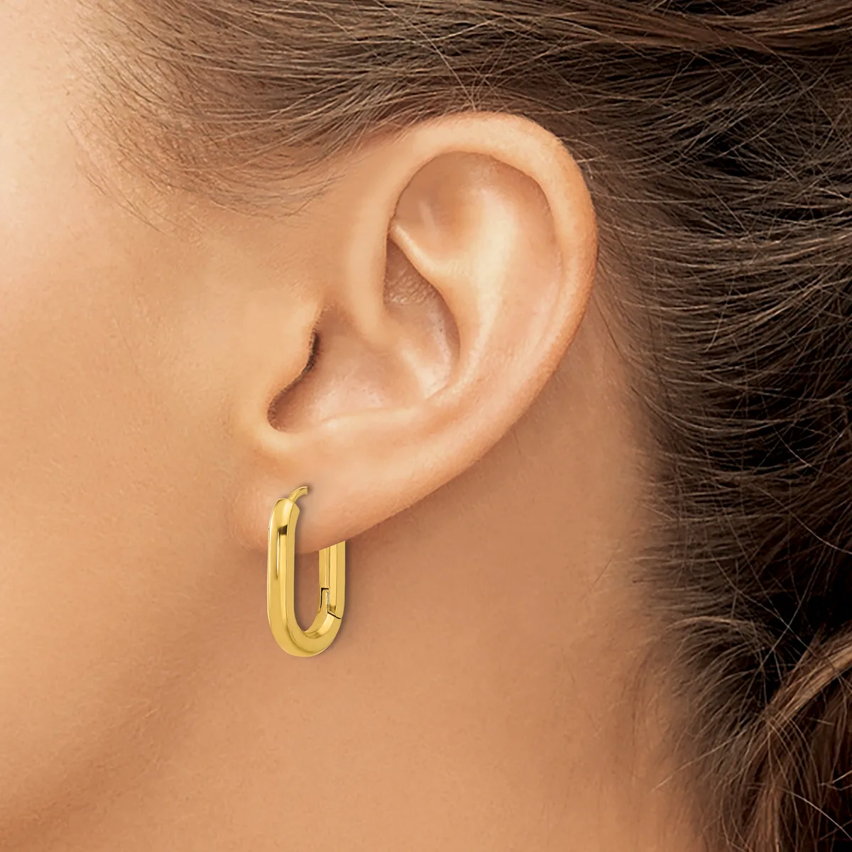 A person wearing a small gold-colored oval hoop earring in their earlobe, shown in profile view.
