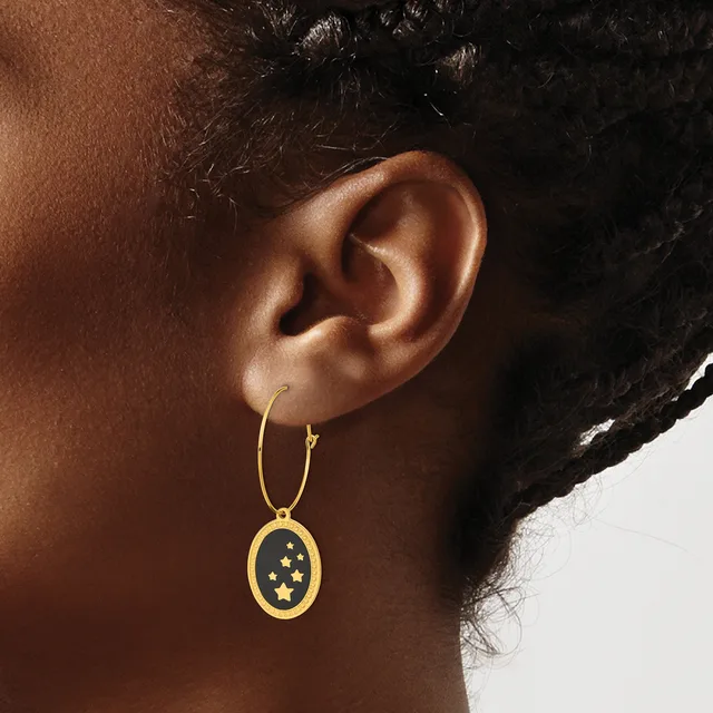 A person wearing a gold hoop earring with a dangling oval pendant featuring stars on a dark background.