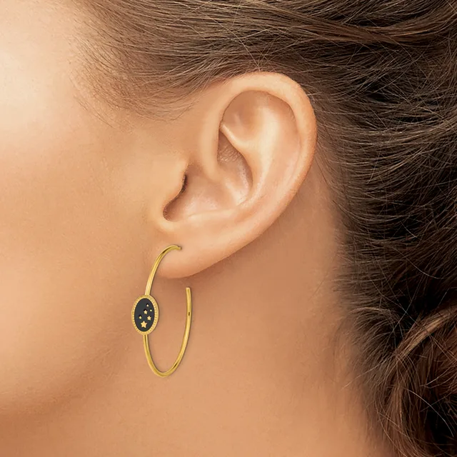 A person wearing gold hoop earrings with a small dark oval pendant charm on one ear, shown in profile against a neutral background.