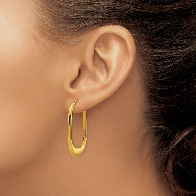 A person wearing a pair of gold-toned oval hoop earrings with a polished finish, shown from the side profile view.