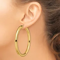A woman wearing large gold hoop earrings with a polished finish, shown from the side view of her ear and neck.