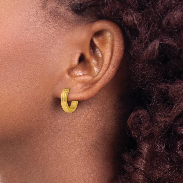 A person wearing a gold hoop earring with a textured surface, shown in profile against their ear and dark curly hair.
