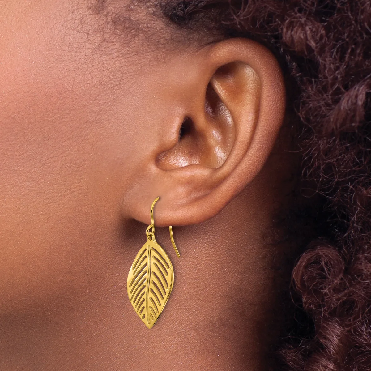 A person wearing a gold leaf-shaped drop earring with detailed vein texturing, shown from the side profile against their neck and shoulder.