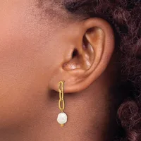 A person wearing a gold chain link earring with a white pearl pendant hanging from the earlobe.