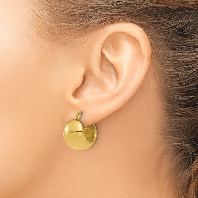 A woman wearing a gold-toned chunky hoop earring with a polished finish, shown from the side view against her ear.