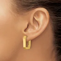 A person wearing a pair of polished gold rectangular hoop earrings with a flat surface and hinged closure, shown from the side view near their ear.