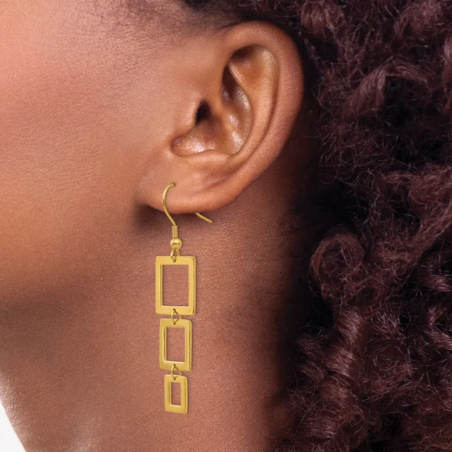 Gold rectangular link drop earrings with a hook closure, shown worn on a person's ear against their shoulder and dark curly hair.