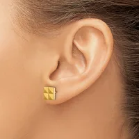 A person wearing a pair of small gold stud earrings with a geometric pyramid or quilted pattern, shown from the side view of their ear.