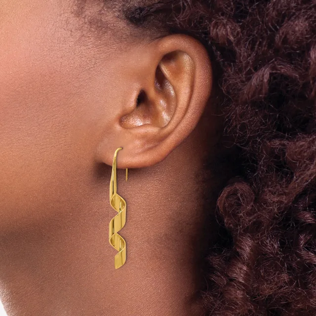 A person wearing a gold twisted drop earring on a fish hook wire, shown from the side against their neck and shoulder with dark curly hair visible.