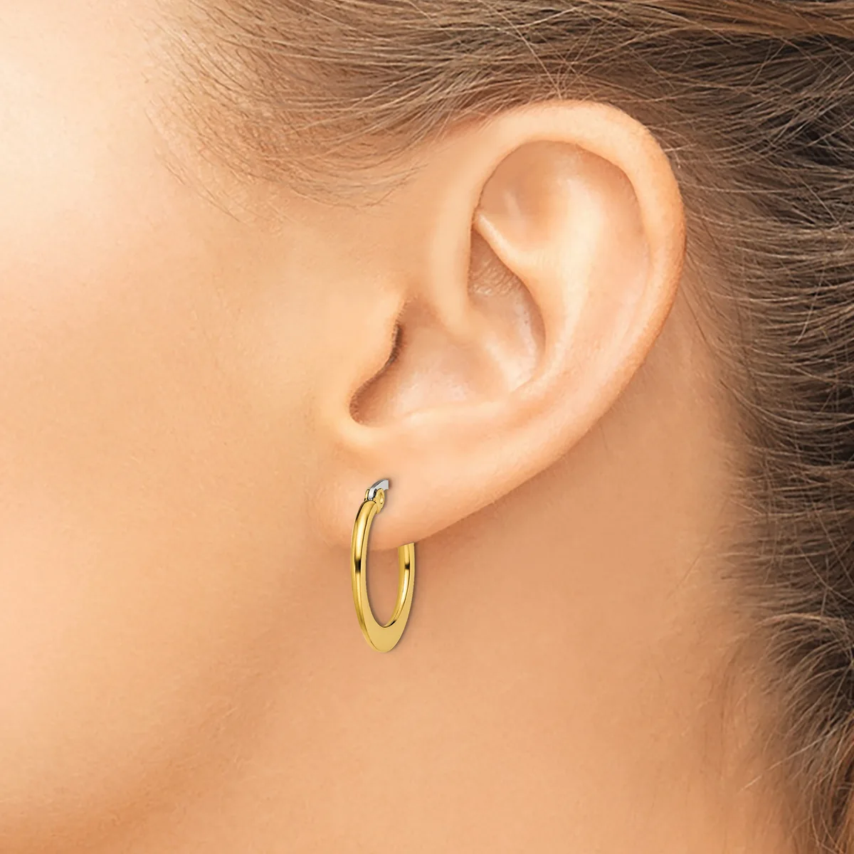 A person wearing a pair of small, polished gold-toned hoop earrings, shown from the side profile of their ear and neck.