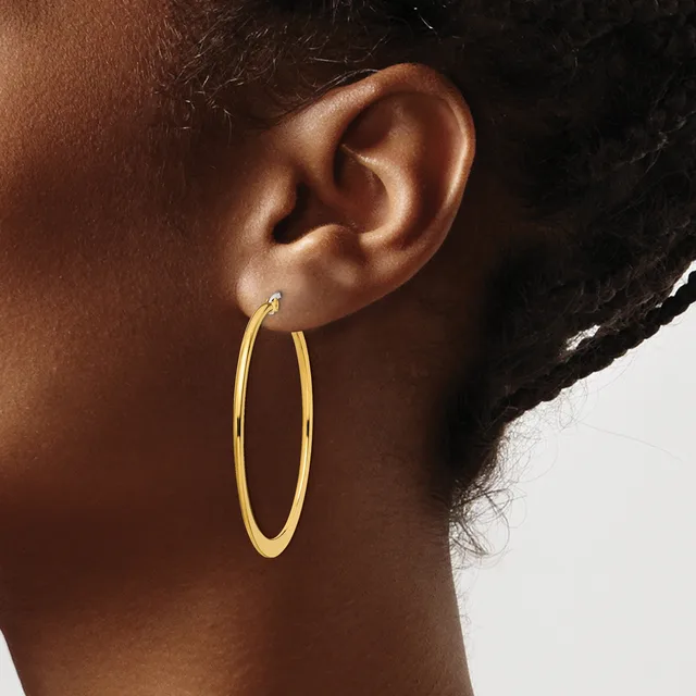 A person wearing a pair of gold hoop earrings, shown in profile from the side of their head and neck against a neutral background.